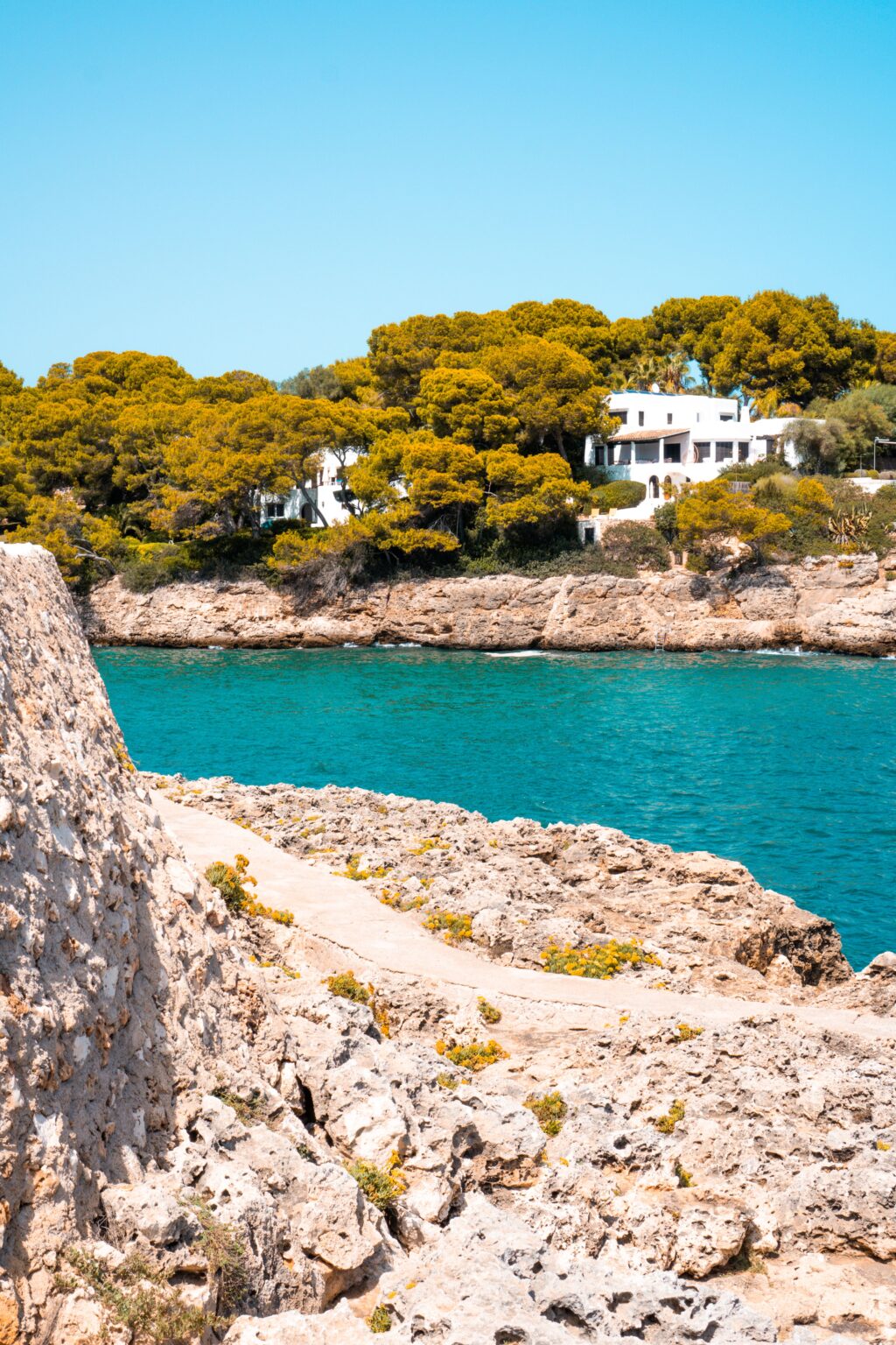 Beautiful Mediterranean villa by turquoise waters surrounded by lush greenery and rocky cliffs.