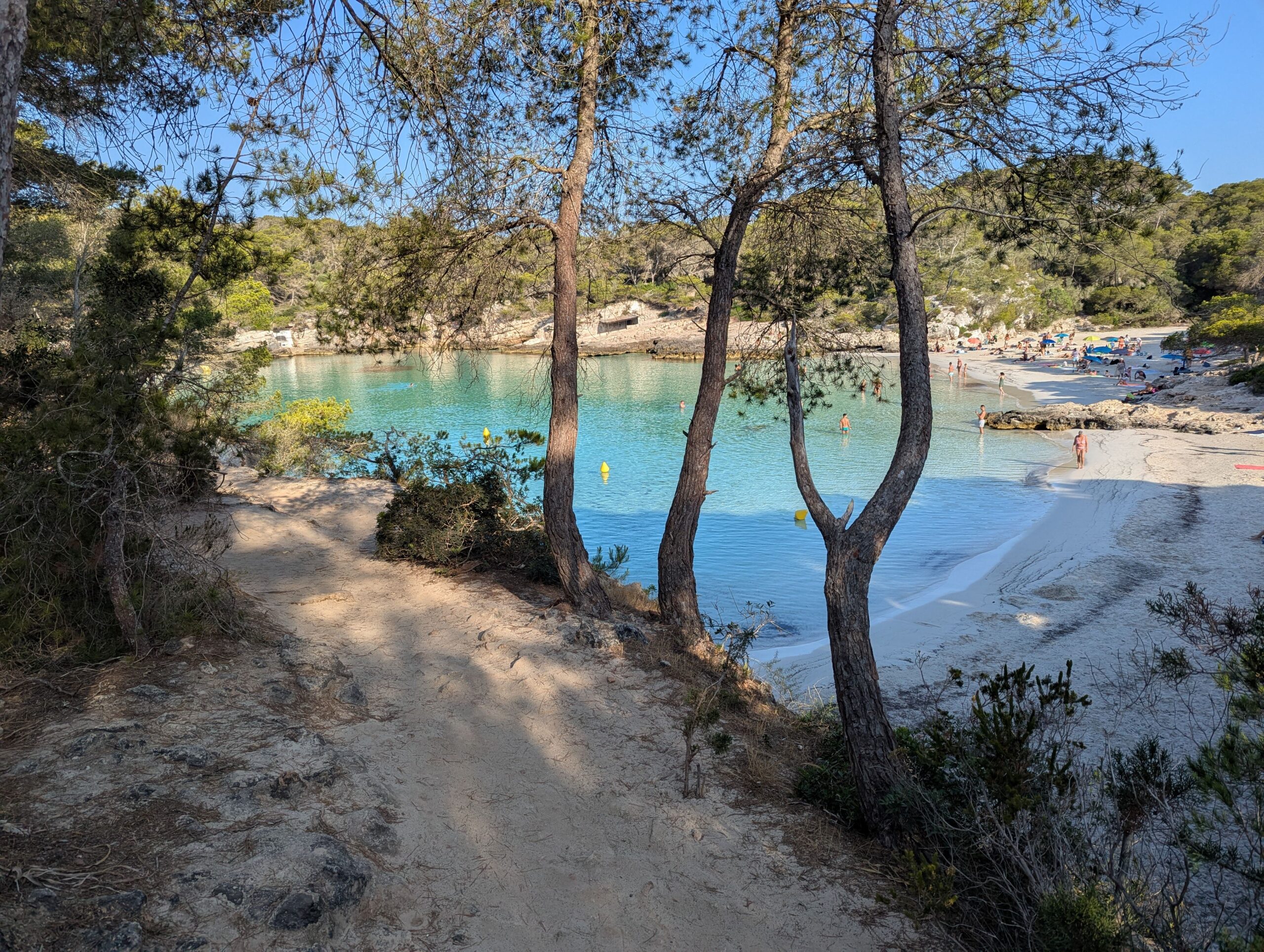 Serene beach scene at Cala Mitjana in Menorca, with clear turquoise waters and sandy shores.